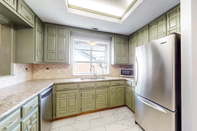 kitchen featuring sink, light stone counters, green cabinets, and appliances with stainless steel finishes