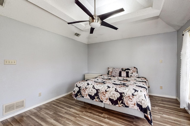 bedroom with wood-type flooring, ceiling fan, and a raised ceiling