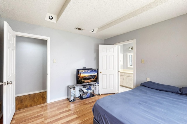 bedroom with light wood-type flooring, a textured ceiling, and ensuite bath