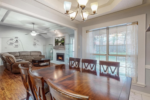 dining area featuring a fireplace, ceiling fan with notable chandelier, and vaulted ceiling