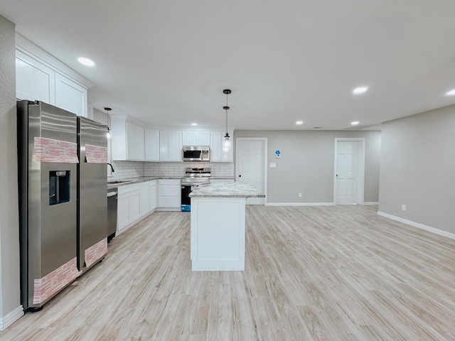 kitchen featuring white cabinetry, light stone counters, decorative light fixtures, a center island, and appliances with stainless steel finishes