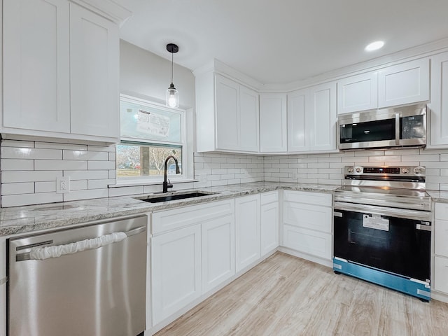 kitchen with decorative light fixtures, sink, white cabinets, stainless steel appliances, and light wood-type flooring