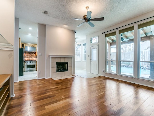 unfurnished living room featuring a tiled fireplace, hardwood / wood-style floors, a textured ceiling, and ceiling fan