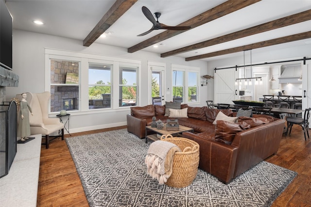 living room featuring dark wood-type flooring, beamed ceiling, ceiling fan, and a barn door