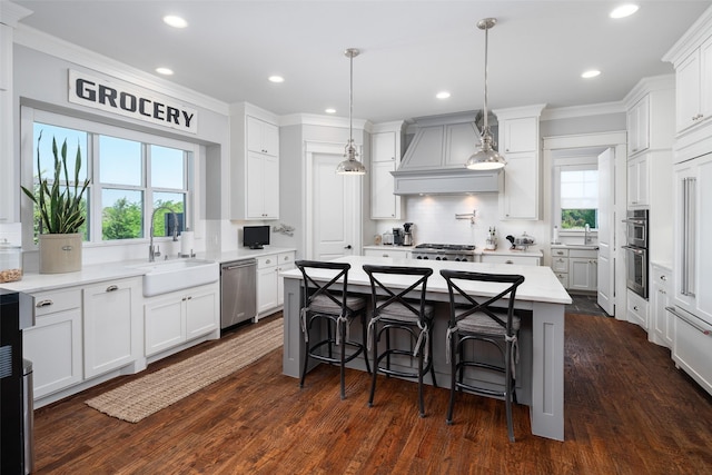 kitchen with custom range hood, appliances with stainless steel finishes, backsplash, white cabinetry, and a kitchen island