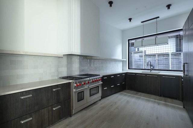 kitchen with light hardwood / wood-style floors, tasteful backsplash, hanging light fixtures, sink, and range with two ovens