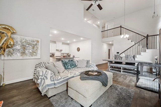 living room featuring dark wood-type flooring, ceiling fan with notable chandelier, and a towering ceiling