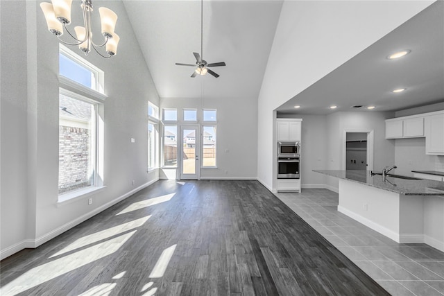 unfurnished living room featuring sink, ceiling fan with notable chandelier, dark tile patterned flooring, and high vaulted ceiling