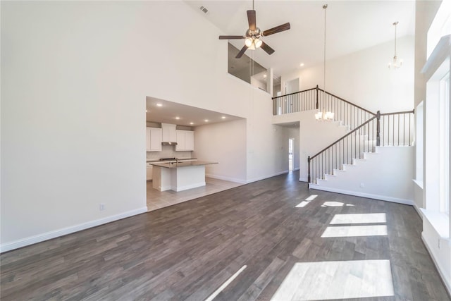 unfurnished living room featuring ceiling fan with notable chandelier, dark hardwood / wood-style floors, and a high ceiling