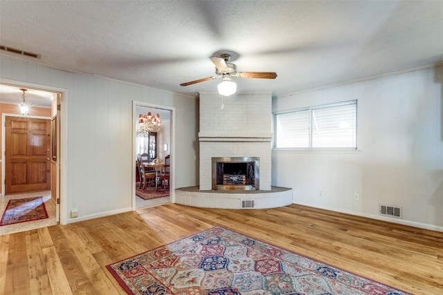 unfurnished living room featuring hardwood / wood-style floors, a textured ceiling, a brick fireplace, ornamental molding, and ceiling fan