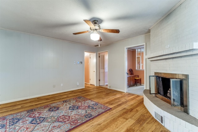 living room with crown molding, light hardwood / wood-style floors, a textured ceiling, a fireplace, and ceiling fan