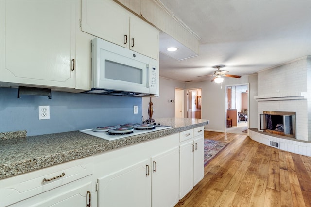 kitchen with white appliances, white cabinets, light hardwood / wood-style flooring, and a fireplace