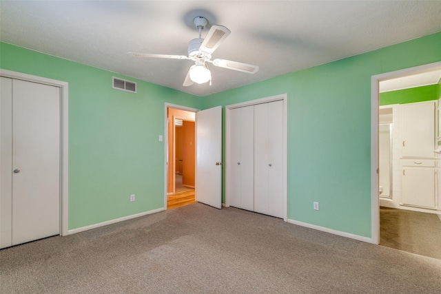 unfurnished bedroom featuring ceiling fan, carpet, ensuite bath, and multiple closets