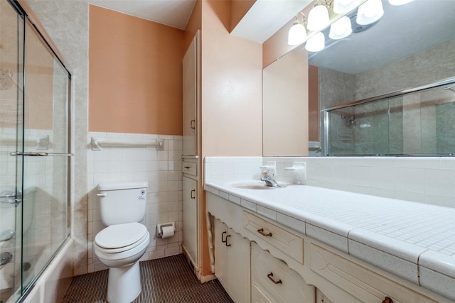 full bathroom featuring toilet, tile walls, shower / bath combination with glass door, tile patterned floors, and vanity