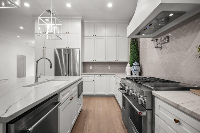 kitchen with sink, premium range hood, white cabinetry, high quality appliances, and light stone countertops