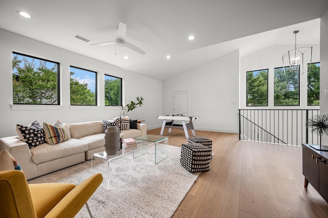 living room with ceiling fan with notable chandelier, light hardwood / wood-style floors, and vaulted ceiling