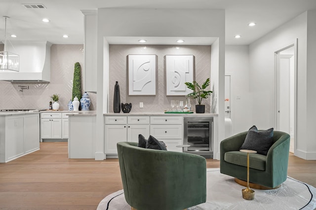 kitchen with custom exhaust hood, white cabinetry, beverage cooler, and backsplash