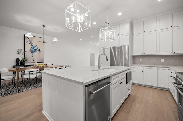 kitchen featuring white cabinetry, an island with sink, premium appliances, and decorative light fixtures