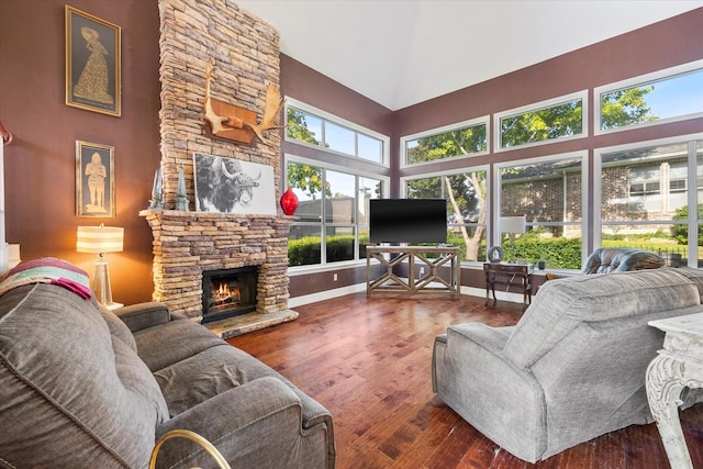 living room featuring dark hardwood / wood-style flooring, a stone fireplace, and a towering ceiling