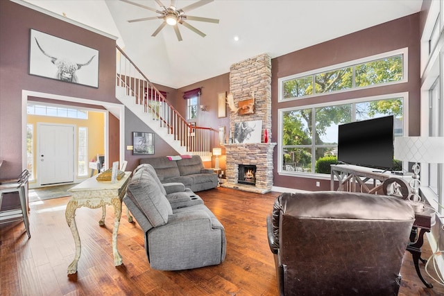 living room with ceiling fan, hardwood / wood-style flooring, high vaulted ceiling, and a stone fireplace