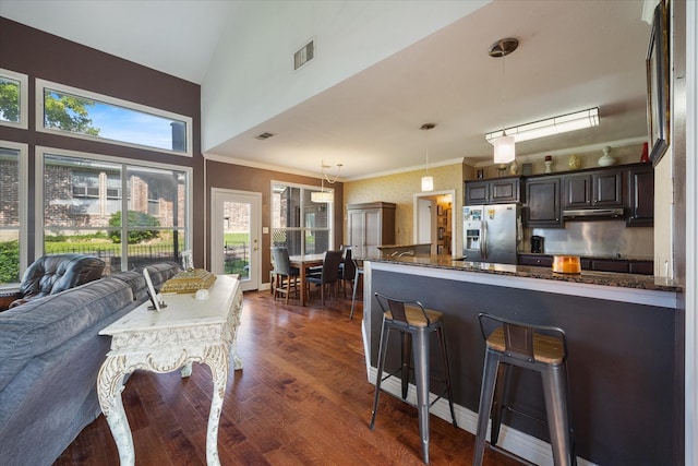 kitchen with pendant lighting, dark wood-type flooring, dark stone countertops, stainless steel fridge with ice dispenser, and dark brown cabinets