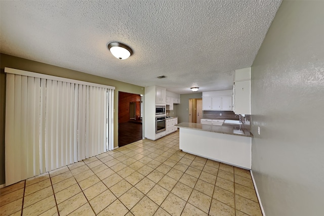 kitchen with a textured ceiling, white cabinetry, stainless steel appliances, sink, and kitchen peninsula