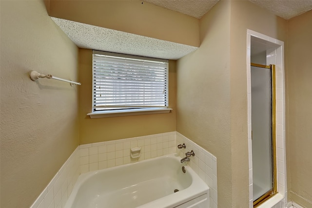 bathroom with a textured ceiling and shower with separate bathtub