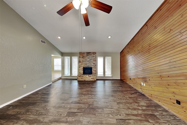 unfurnished living room featuring dark hardwood / wood-style flooring, a fireplace, wood walls, vaulted ceiling, and ceiling fan