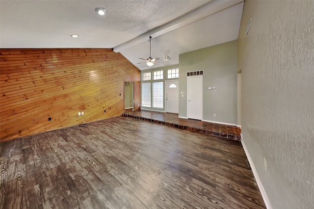 unfurnished living room with a textured ceiling, wood-type flooring, beamed ceiling, wood walls, and ceiling fan