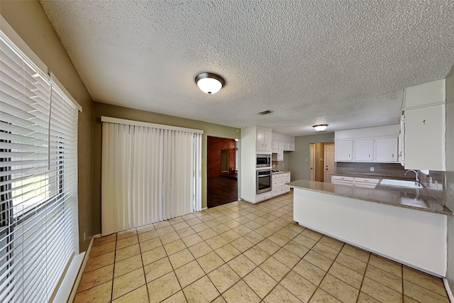 kitchen featuring kitchen peninsula, sink, white cabinets, light tile patterned flooring, and stainless steel appliances