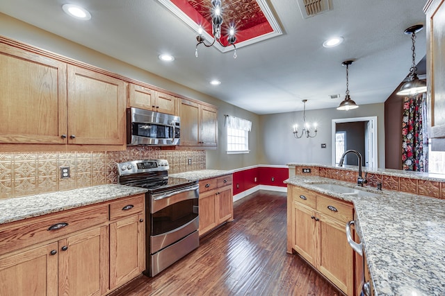 kitchen featuring light stone countertops, hanging light fixtures, sink, backsplash, and stainless steel appliances