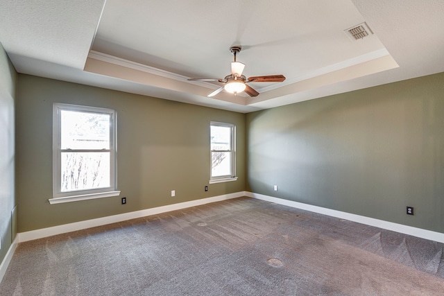 carpeted empty room with ceiling fan, ornamental molding, and a raised ceiling