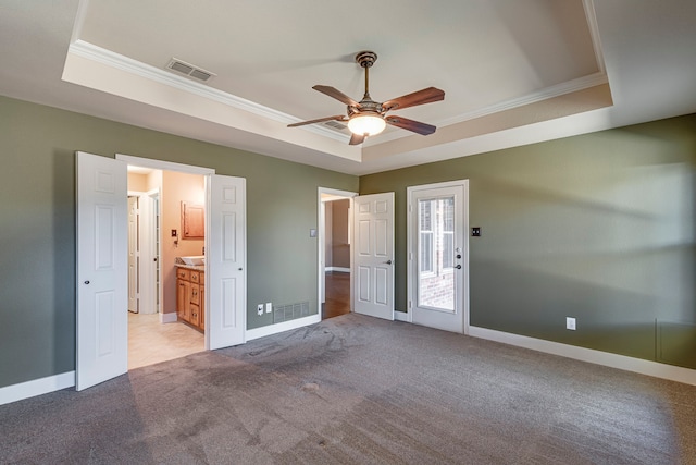 unfurnished bedroom featuring ensuite bathroom, crown molding, a raised ceiling, light colored carpet, and ceiling fan