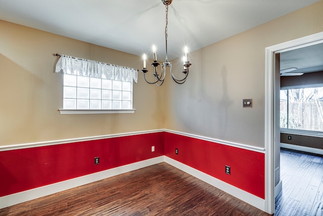 spare room featuring a healthy amount of sunlight, an inviting chandelier, and dark wood-type flooring