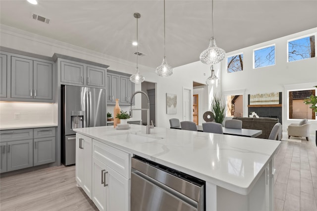 kitchen with sink, decorative light fixtures, an island with sink, stainless steel appliances, and light stone countertops