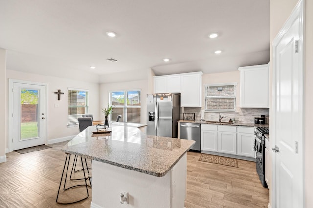 kitchen with sink, white cabinets, light stone counters, a center island with sink, and stainless steel appliances