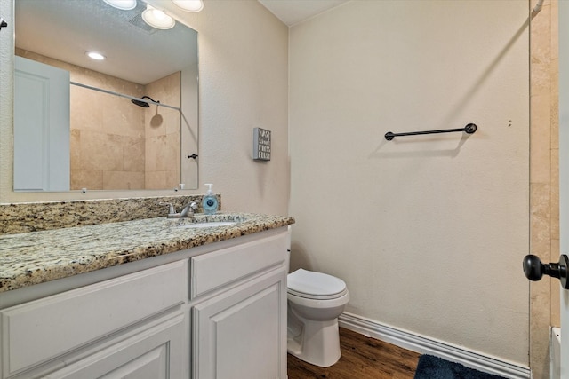 bathroom with hardwood / wood-style flooring, vanity, toilet, and a tile shower