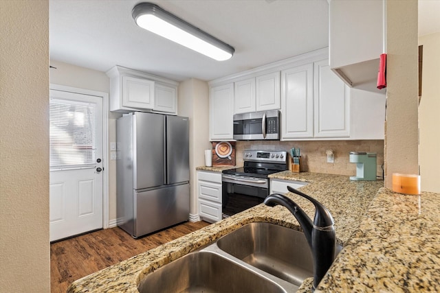 kitchen with appliances with stainless steel finishes, dark hardwood / wood-style floors, white cabinetry, sink, and backsplash