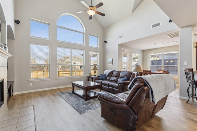 living room with high vaulted ceiling, ceiling fan with notable chandelier, a tile fireplace, and light wood-type flooring