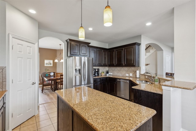 kitchen featuring appliances with stainless steel finishes, decorative light fixtures, sink, light stone counters, and kitchen peninsula