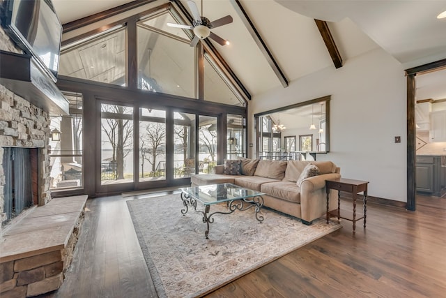 living room with a stone fireplace, high vaulted ceiling, beam ceiling, ceiling fan with notable chandelier, and dark hardwood / wood-style floors