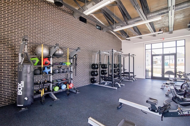 exercise room featuring a towering ceiling, brick wall, and french doors