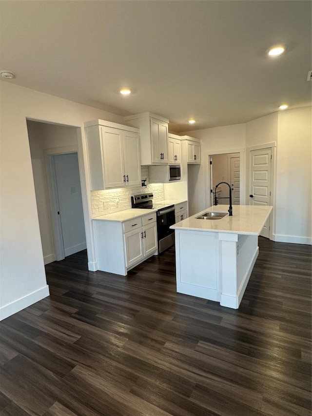 kitchen featuring appliances with stainless steel finishes, white cabinetry, sink, backsplash, and a center island with sink