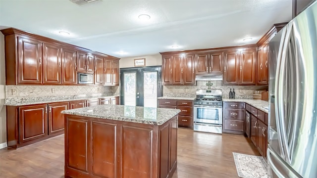 kitchen featuring light hardwood / wood-style flooring, tasteful backsplash, light stone countertops, a kitchen island, and stainless steel appliances