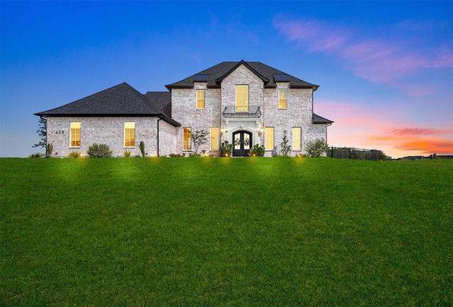 french country style house with french doors, a balcony, and a lawn