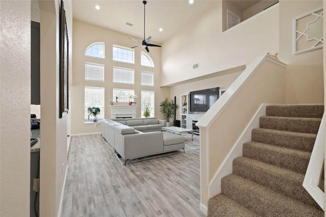 living room with a towering ceiling, ceiling fan, and light hardwood / wood-style flooring