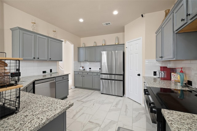 kitchen with gray cabinets, tasteful backsplash, light stone countertops, and appliances with stainless steel finishes