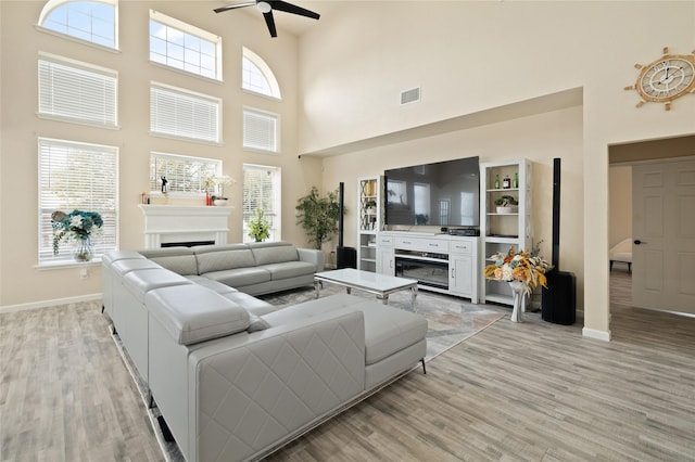 living room with ceiling fan, a high ceiling, and light wood-type flooring