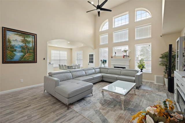 living room featuring light hardwood / wood-style floors, a towering ceiling, and ceiling fan