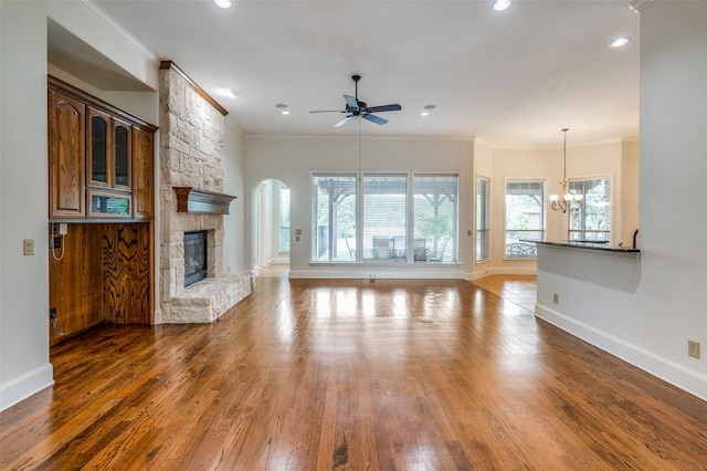 unfurnished living room featuring ceiling fan with notable chandelier, dark hardwood / wood-style flooring, ornamental molding, and a stone fireplace